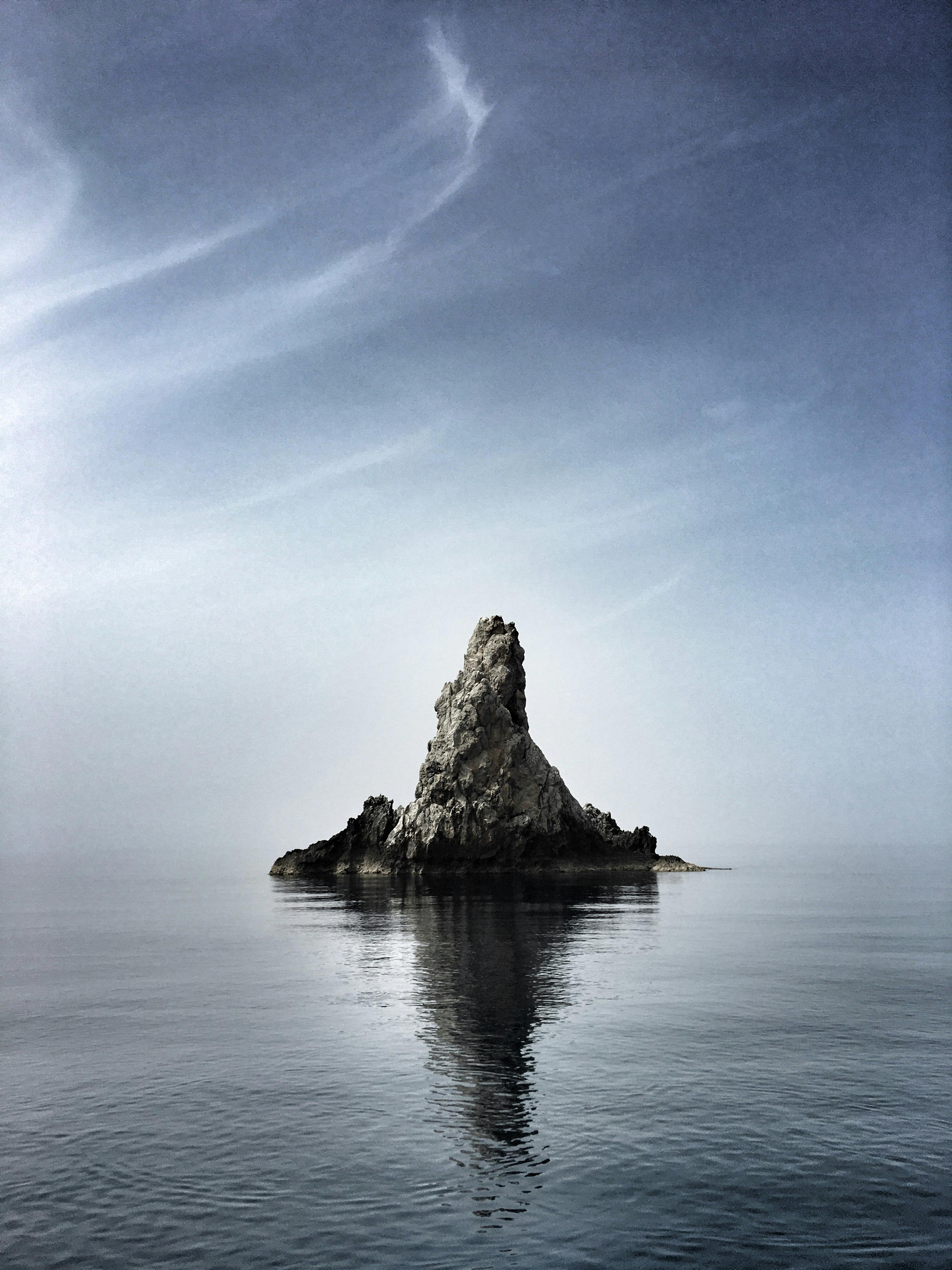Distant stony steep cliff located in calm rippling water surface under clear sky
