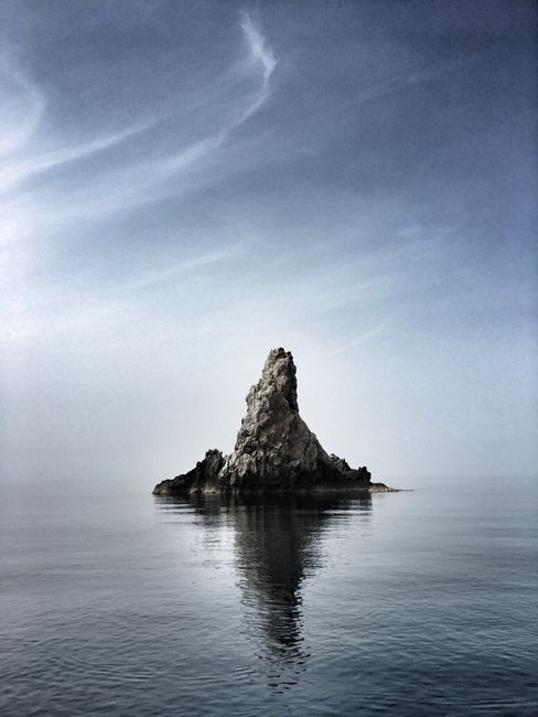 Distant stony steep cliff located in calm rippling water surface under clear sky