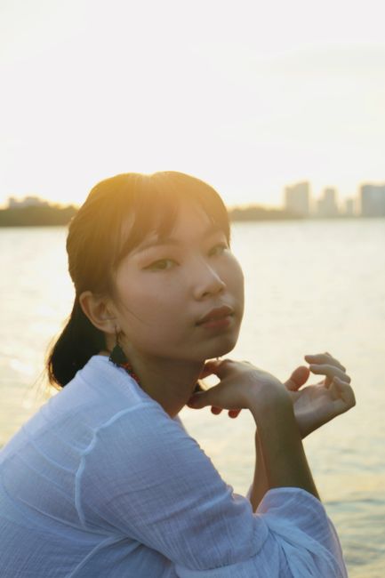 Side view of tranquil Asian female sitting neat calm river and relaxing at sunset