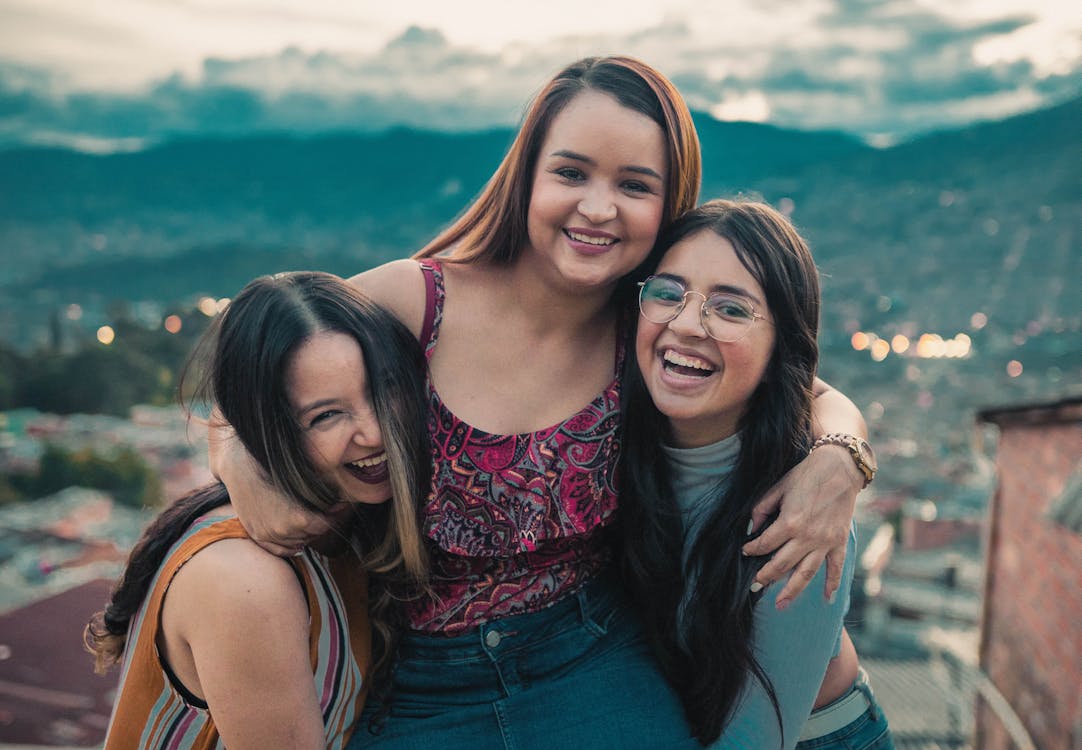 Group of cheerful females embracing on roof of building while spending time together