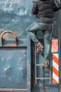 Person in Blue Denim Jeans and Black Leather Boots Standing Beside Blue and Red Metal Door