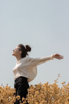 一名妇女穿着白衬衫，在春天的黄色花田里享受户外活动