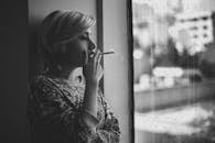 一名短发黑人和一名白人抑郁女性抽着烟，望着窗外雨中的城市