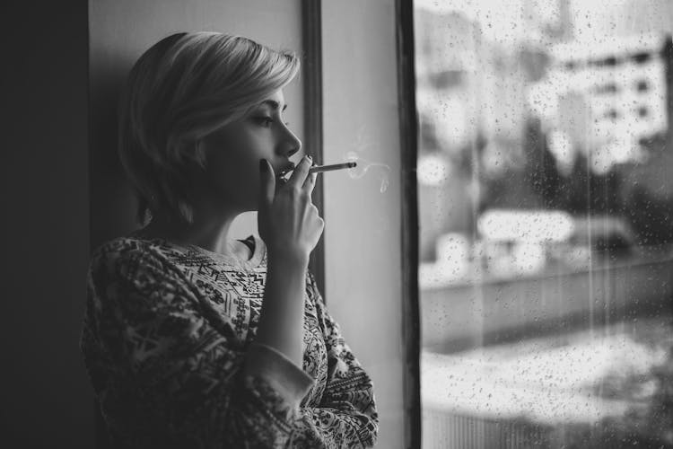 Melancholic Woman Smoking Cigarette Near Window During Rain