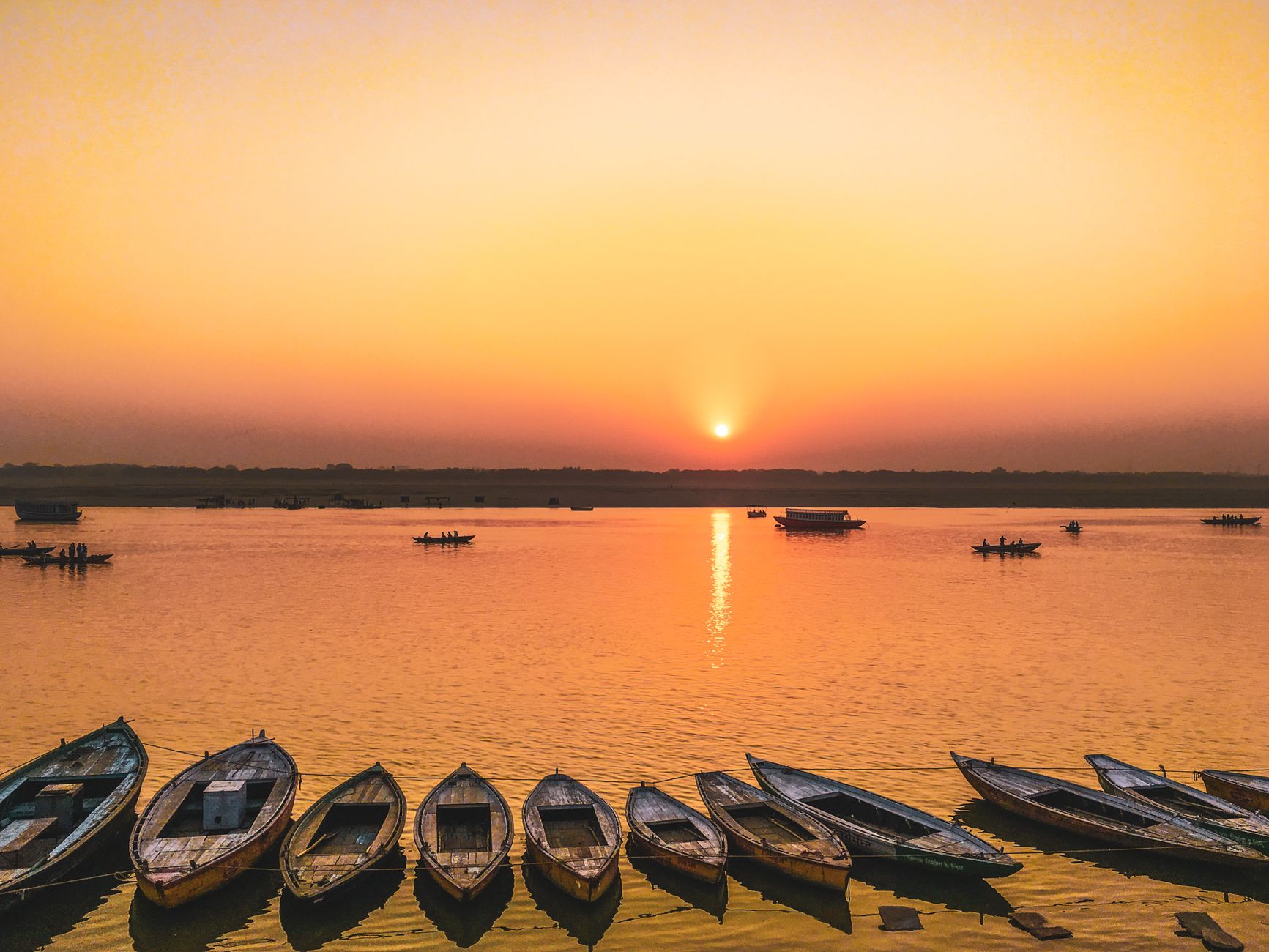 Scenic sunset view over the Ganges River with wooden boats reflecting the warm orange sky.