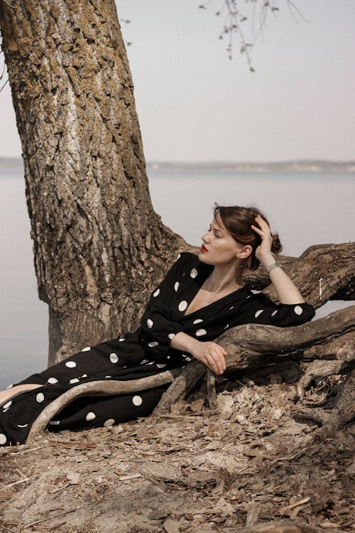 Woman in Black and White Polka Dot Dress Sitting on Brown Tree Trunk