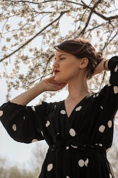 一位黑发女子身穿黑色圆点连衣裙，在盛开的树下享受春天的艺术肖像