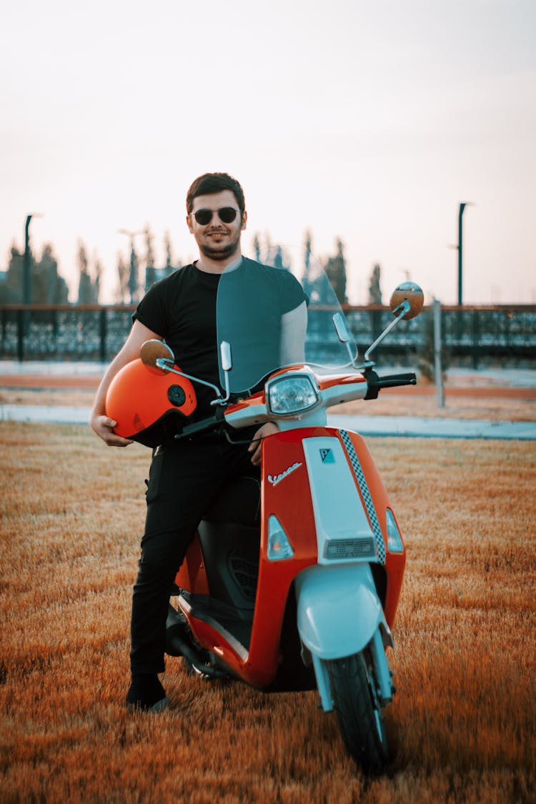 Man In Black Sweater Riding Red Motor Scooter Holding Orange Helmet