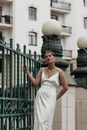 Woman in White Spaghetti Strap Dress Standing Beside Blue Metal Fence