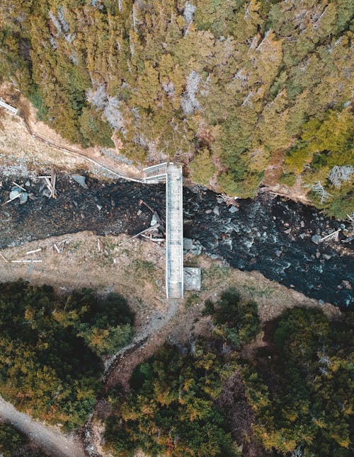 Drone top view of narrow white footbridge above fast stream between shores covered with coniferous forest