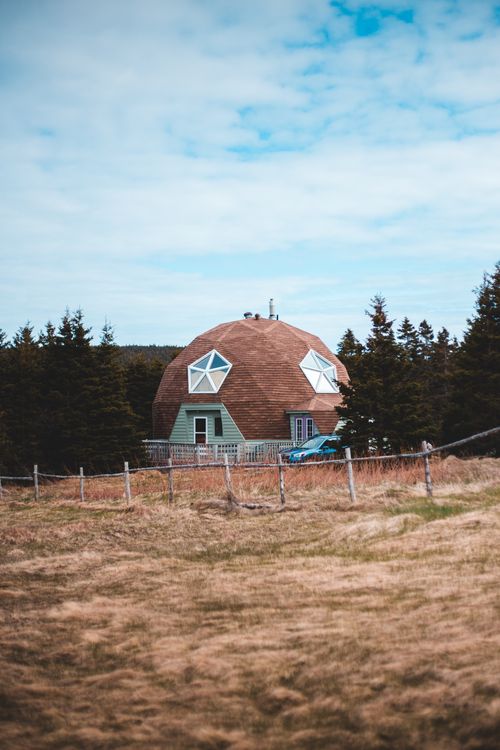 Free Exterior of creative contemporary residential house with poly angular piled roof of brown color and star shaped window located on grassy valley amidst firs and rural fence Stock Photo