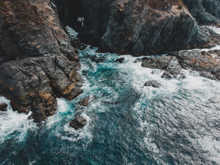 High angle crystal clear turquoise seawater splashing over rough rocky coast in daylight