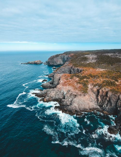 Free Drone view amazing scenery of calm turquoise seawater splashing over rough cliffs with dry vegetation on clear day Stock Photo