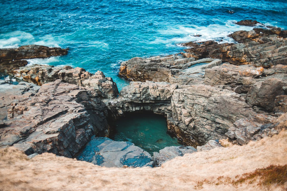 From above of amazing waving turquoise ocean with rocky cliffs and grotto on sunny day