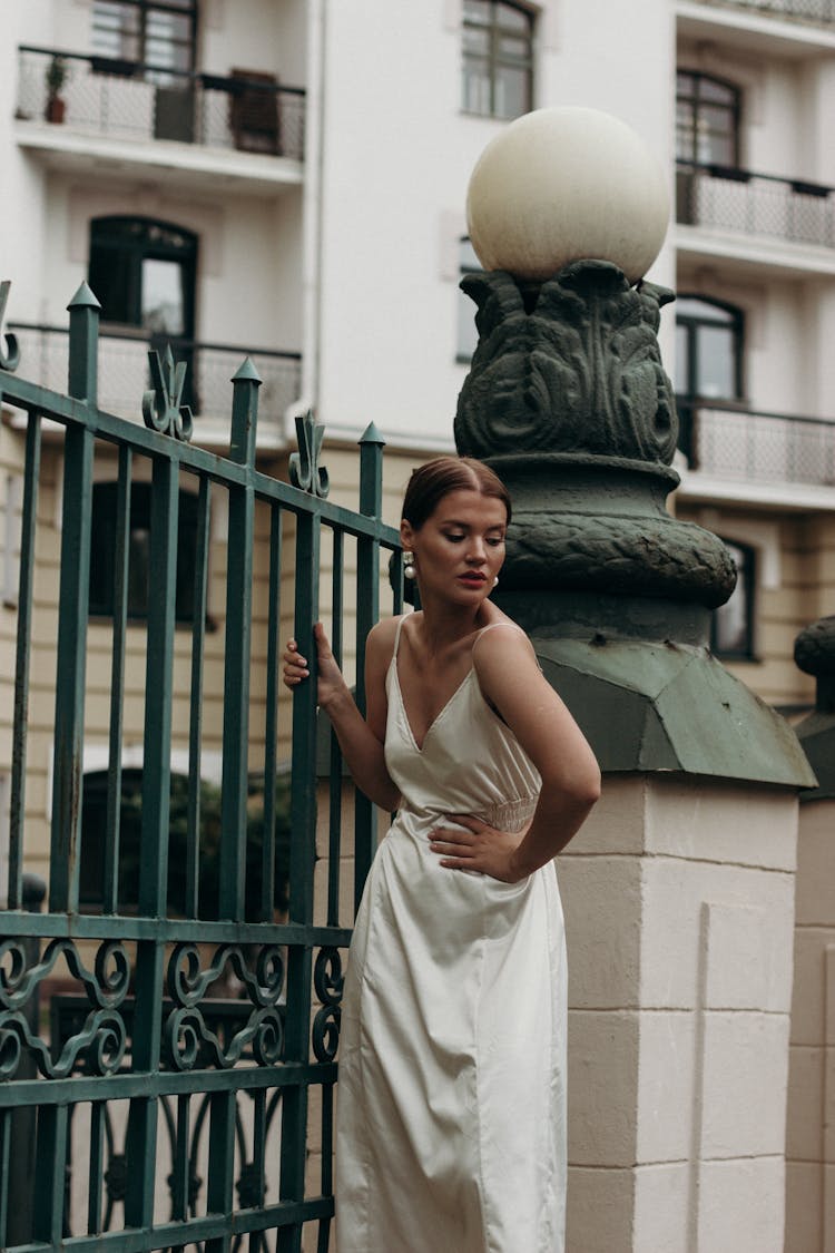 A Woman In Beige Dress Holding A Steel Fence
