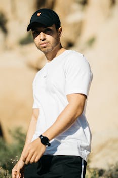 Self confident young unshaven ethnic male in sportive outfit standing in field on sunny day