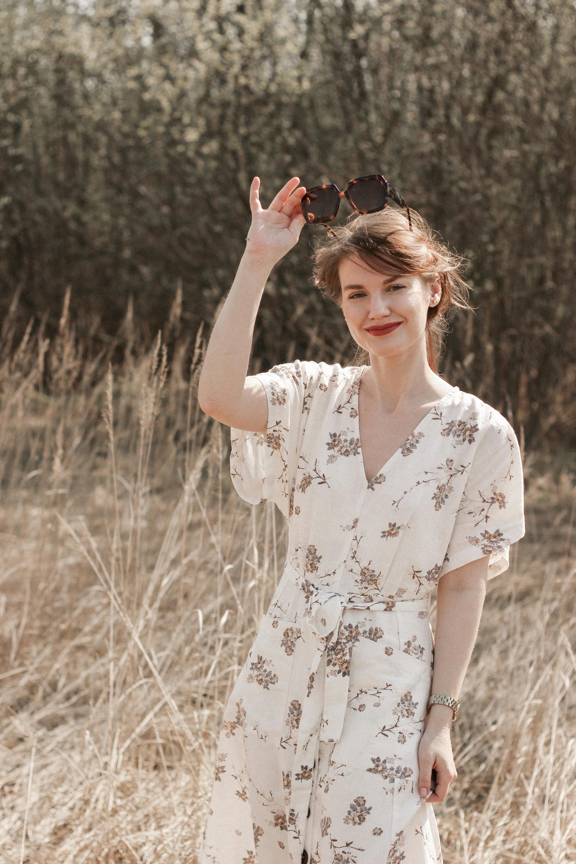 阳光明媚的草地上，一位穿着花卉连衣裙、戴着太阳镜的女人微笑着