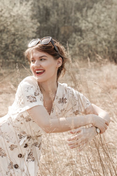 Woman in White Floral Dress Smiling in Brown Grass Field