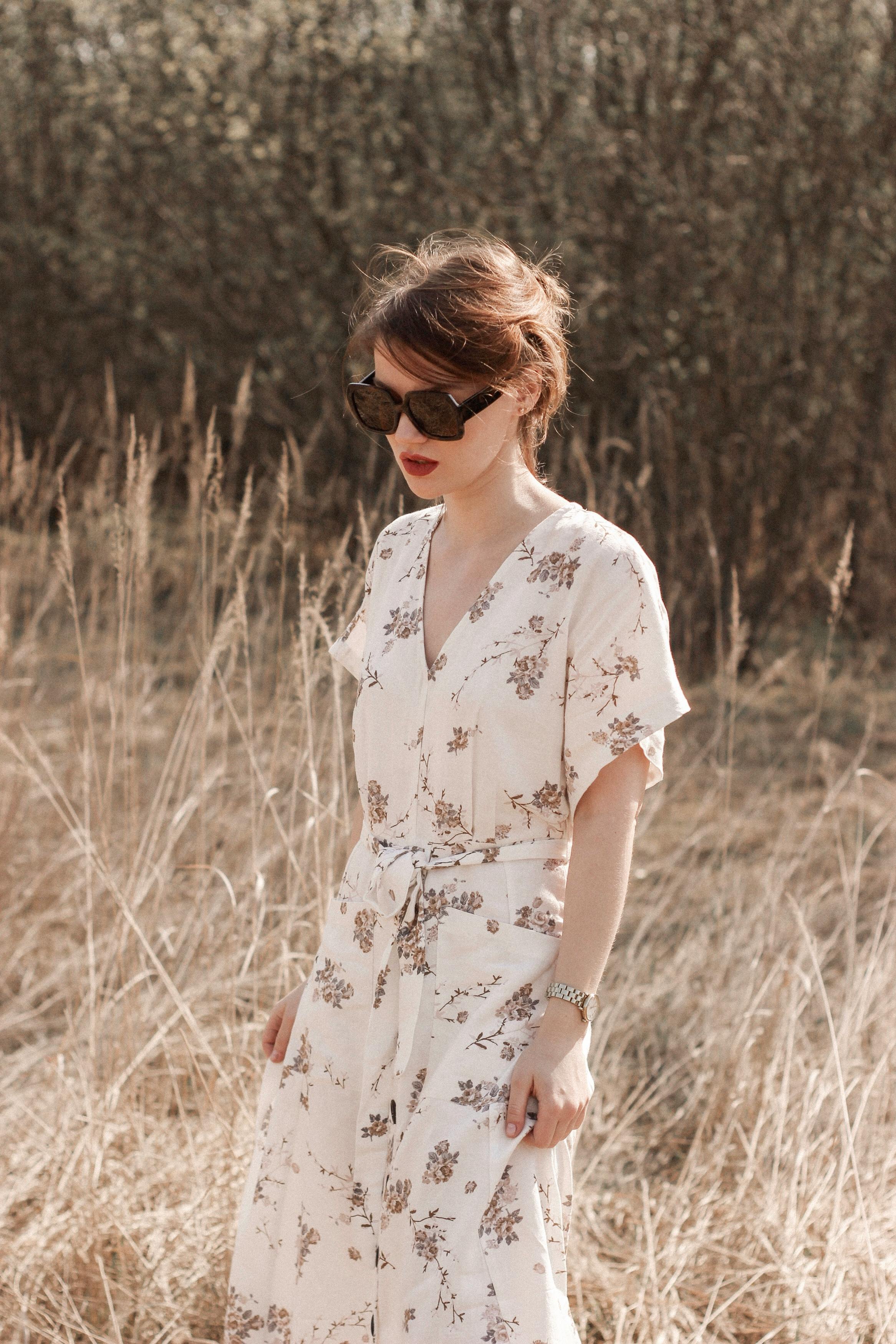 一位戴着太阳镜、身穿花卉连衣裙的时尚女人站在田野里