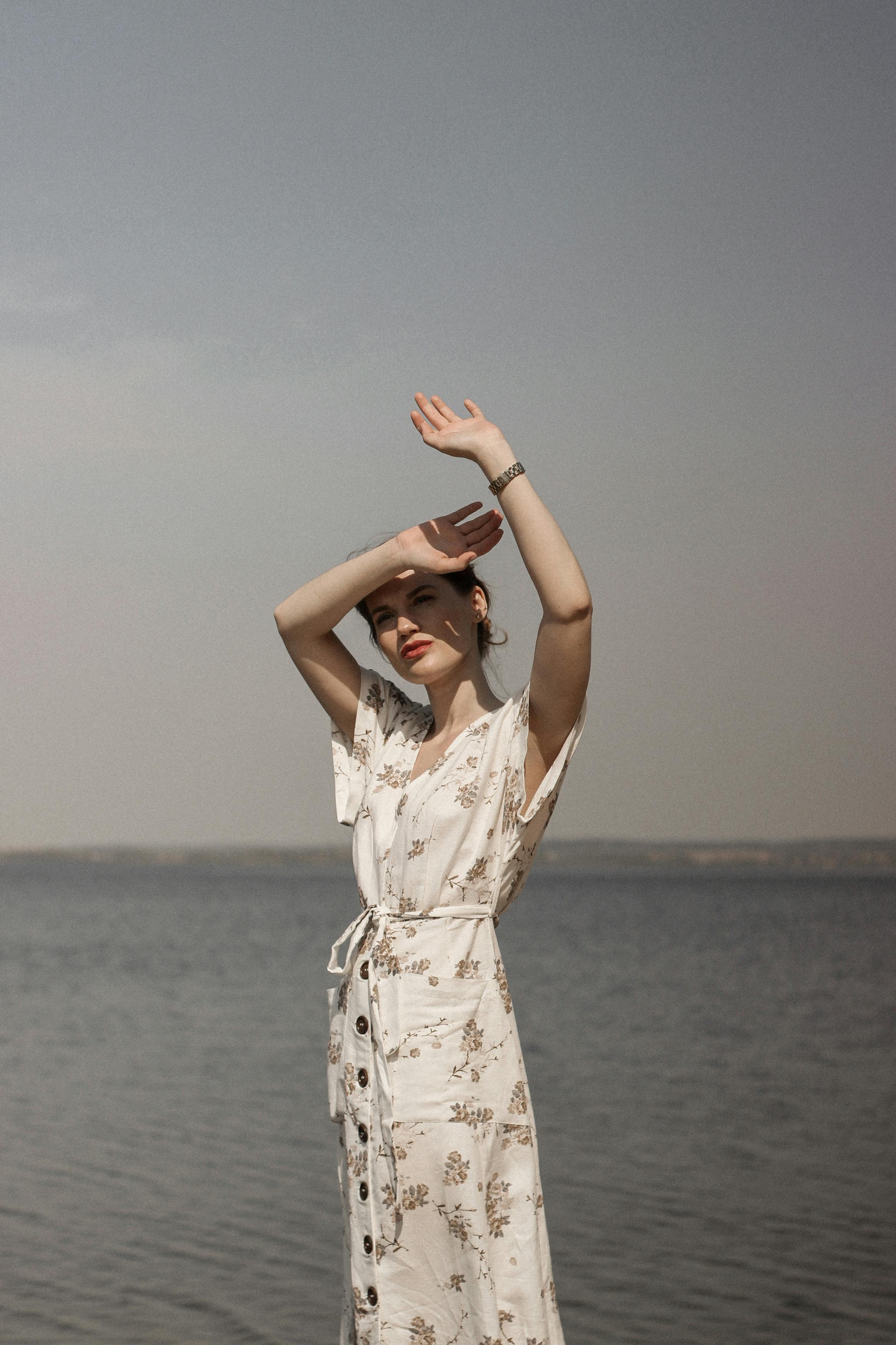 穿着花卉连衣裙的年轻女子站在海边，享受着阳光明媚的一天