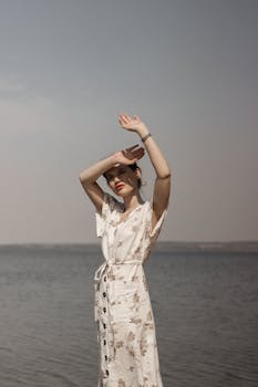 一位身着花卉连衣裙的年轻女子站在海边，享受着阳光明媚的一天