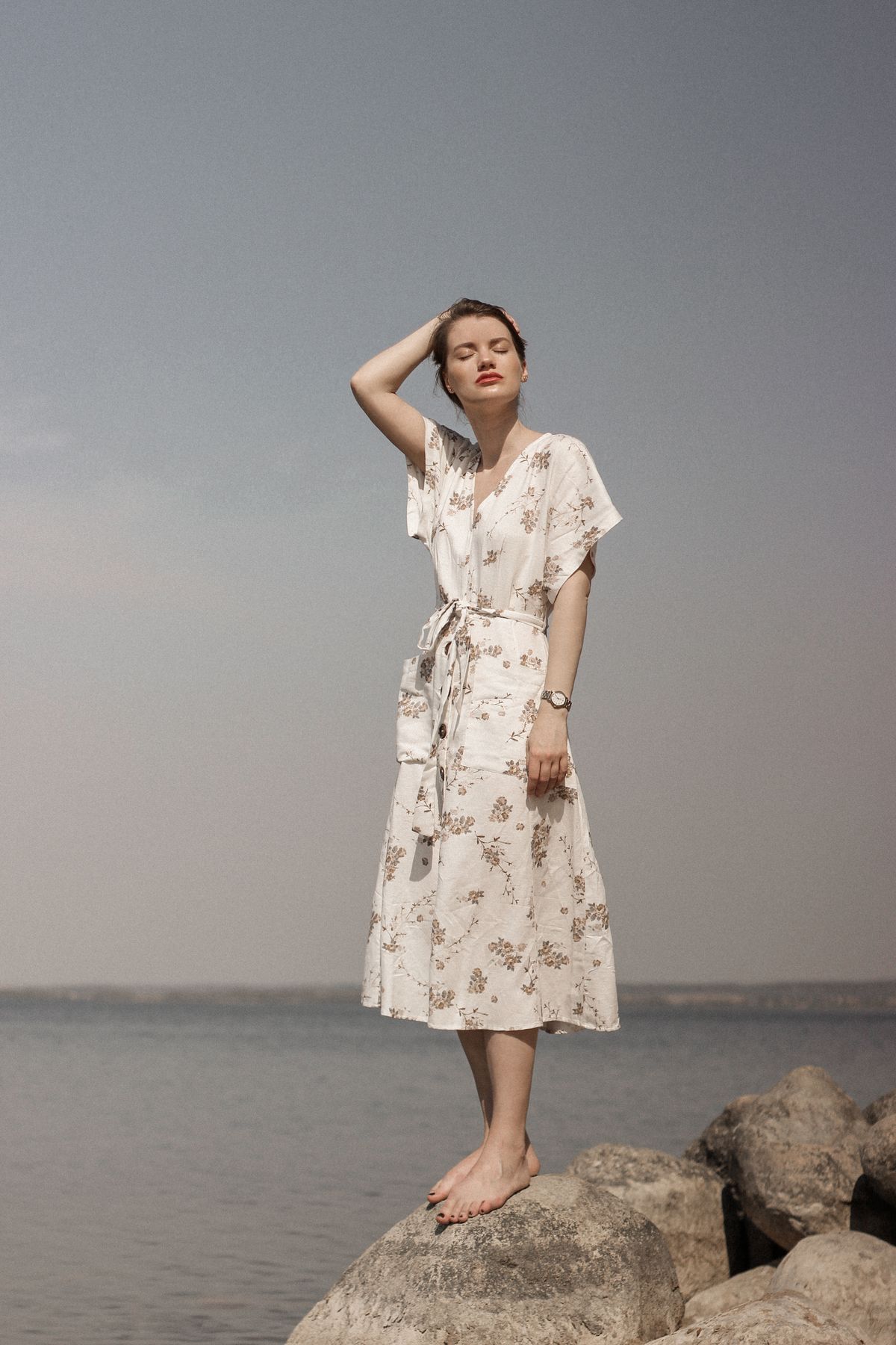 A woman touching her hair, posing in a delicate floral dress
