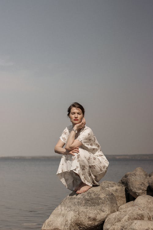 Woman in Floral Dress Sitting on Rock Near Sea