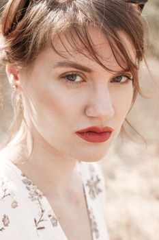 Close-up portrait of a woman outdoors with floral attire, showcasing natural beauty with red lipstick.