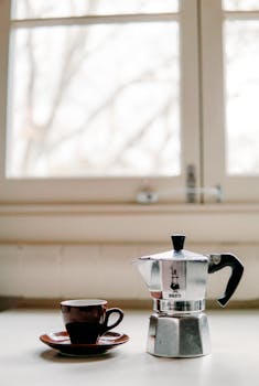 Retro metal geyser coffee maker placed on white table with ceramic cup in light kitchen