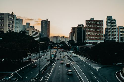 Free Various vehicles riding along asphalt road near modern buildings in city district against sunset sky Stock Photo