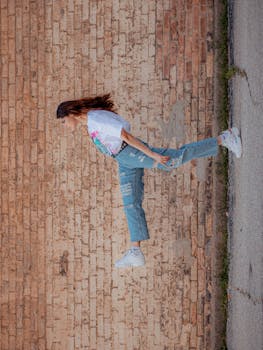 Fashionable woman posing against a brick wall, showcasing denim jeans and sneakers style.