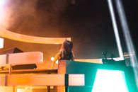 Low angle of young female DJ in headphones on neck recording song standing on stage with neon illumination and spotlights during party in nightclub