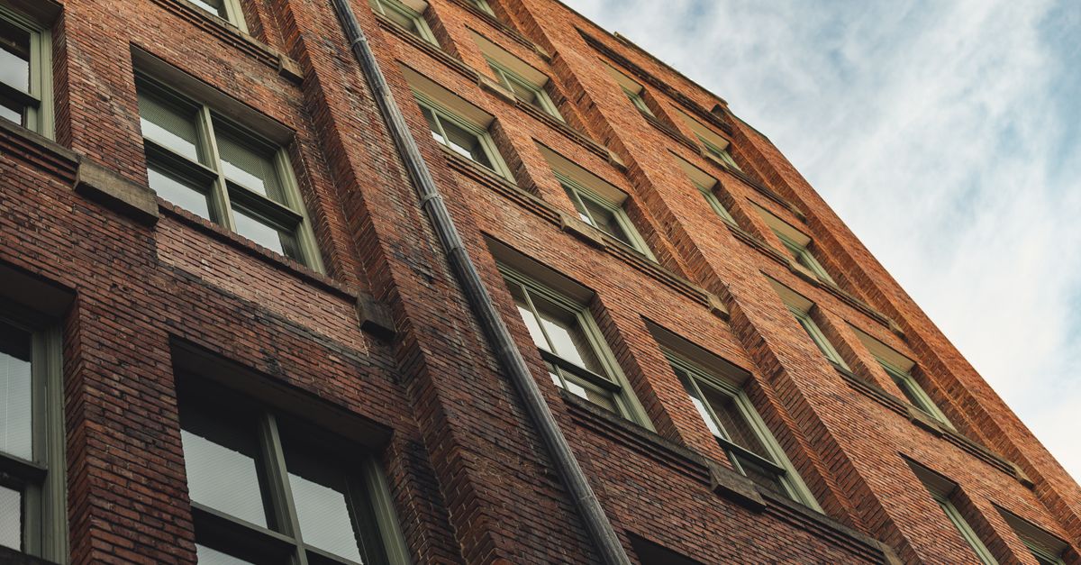 From below of modern building facade with brick walls and windows against cloudy blue sky