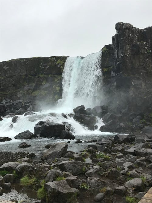 Low angle of powerful waterfall streaming through rocky cliff and flowing into wild river in Thingvellir National Park located in Iceland