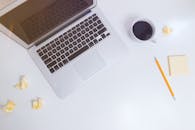 这是一张极简主义工作空间的顶视图，上面摆放着笔记本电脑、咖啡杯、铅笔和一张皱巴巴的纸