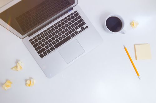 Free Top view of a minimalist workspace with a laptop, coffee cup, pencil, and crumpled paper. Stock Photo