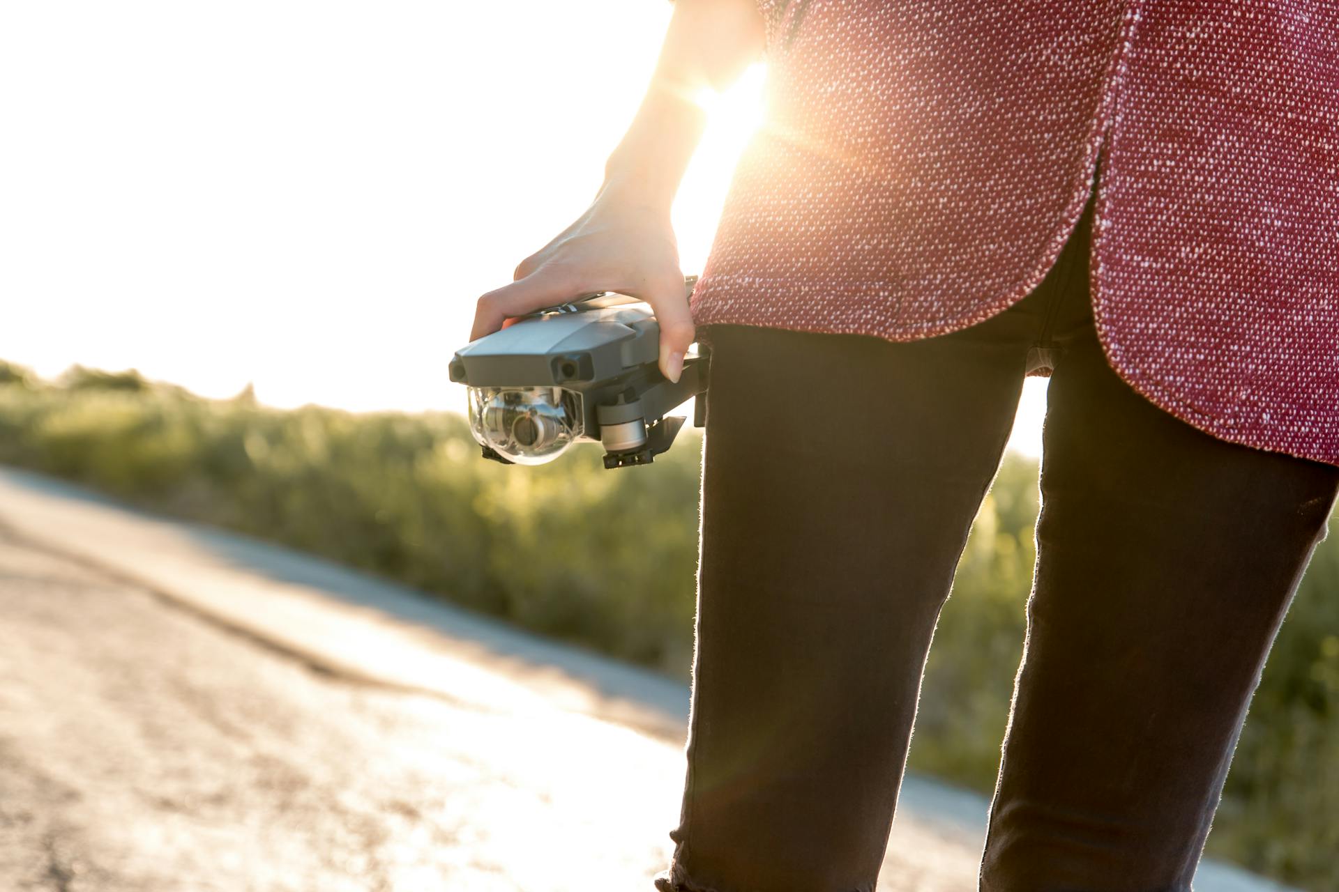 A woman holding a drone on a sunny road, embodying modern technology and adventure.