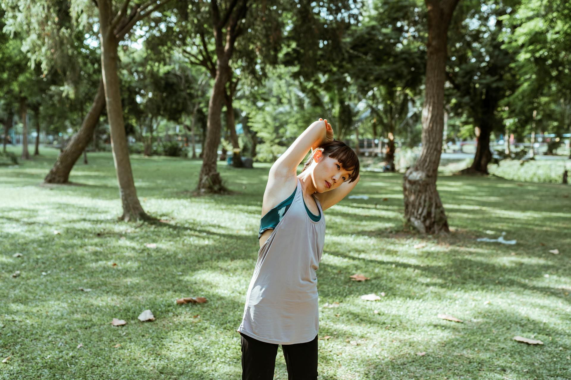 Focused Asian female athlete in activewear doing stretching exercise for legs and back alone in park in daytime