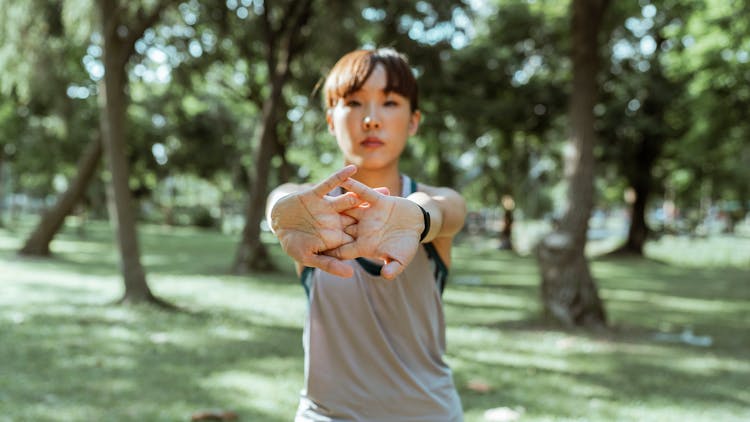 Asian Female Athlete Stretching Arms On Lawn