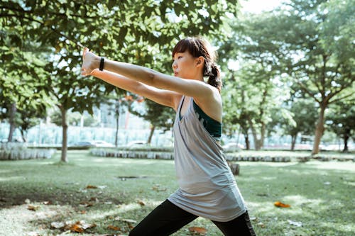Side view of concentrated young Asian lady in sportswear doing stretching exercises while training alone in green sunny park