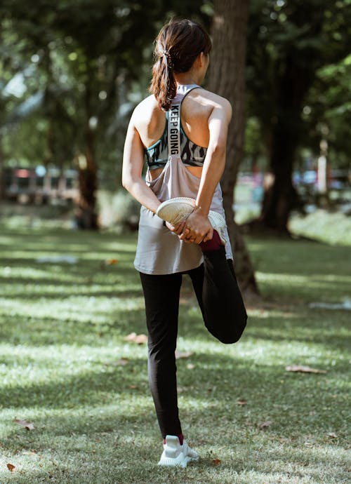 Free Back view full length anonymous female in sportswear stretching legs before exercising while training in sunny summer park Stock Photo