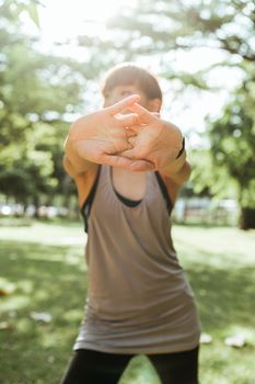 夏日清晨，阳光明媚，一位身材苗条、面目全非的女性在公园健身锻炼，她穿着黑色紧身裤和灰色运动上衣，伸展着手臂
