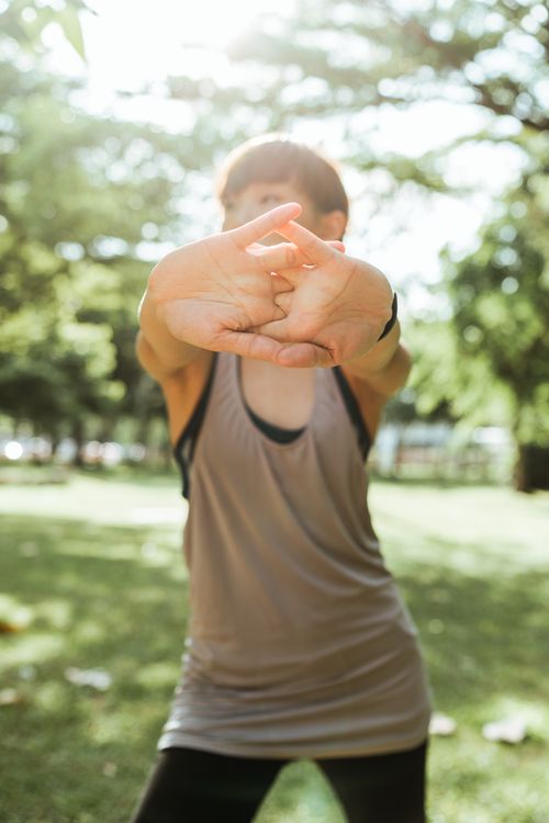 Free Unrecognizable slim female in back lit wearing black leggings and gray sports top stretching arms during fitness workout on sunny summer morning in park Stock Photo