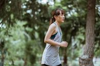 夏日阳光明媚，一名年轻女子慢跑穿过郁郁葱葱的绿色公园