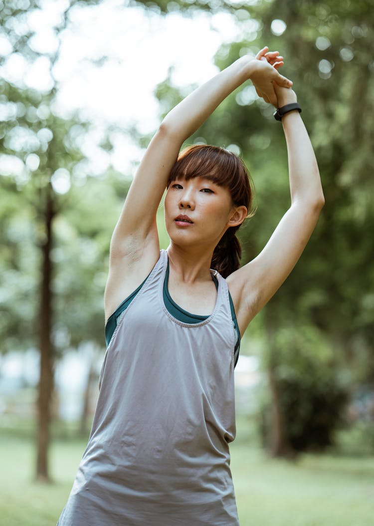 Sporty Asian Sportswoman Stretching Arms During Workout In Forest