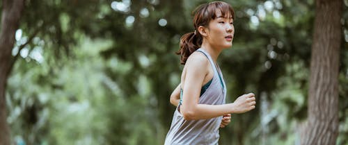 Positive Asian sportswoman jogging in countryside