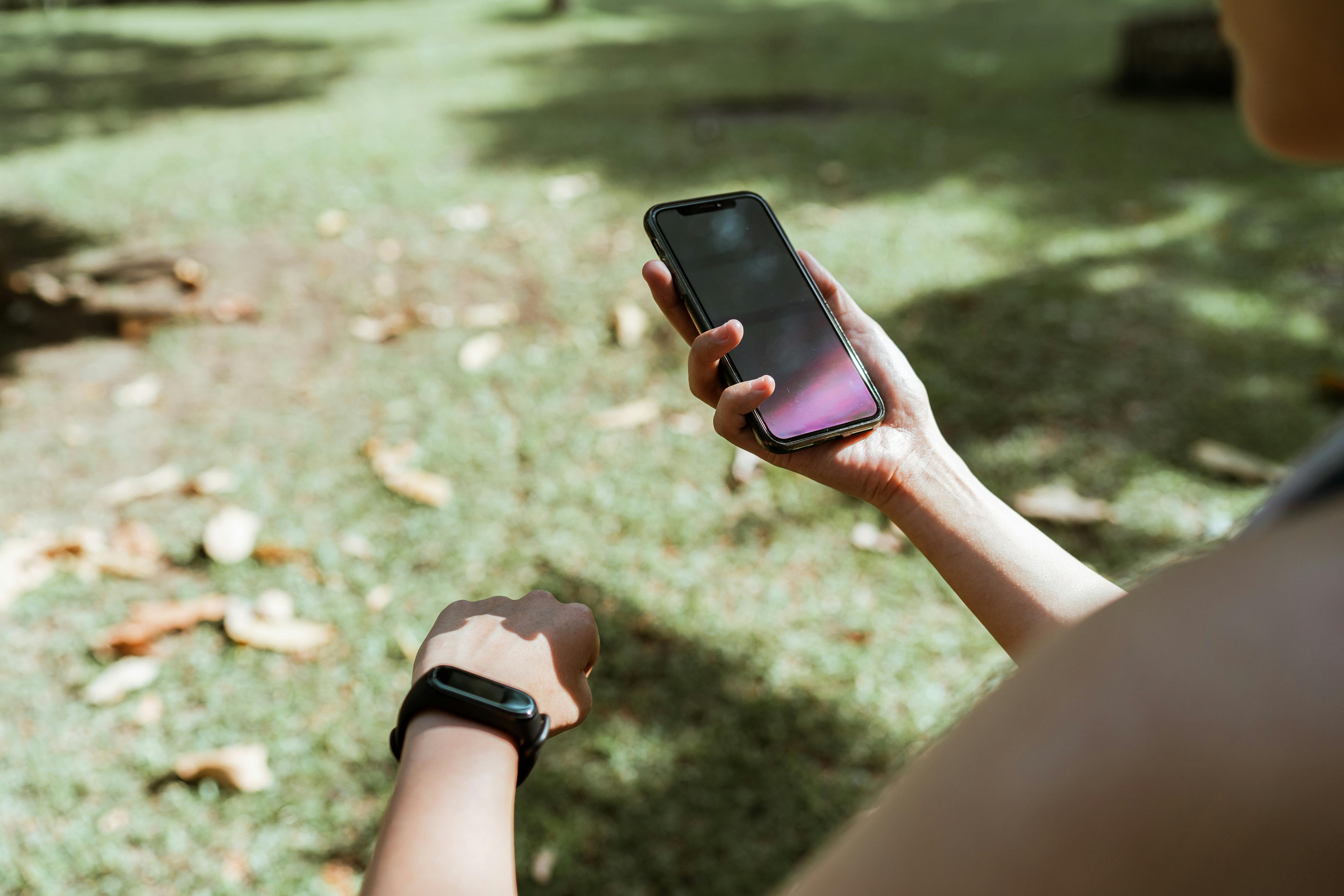 crop woman with fitness bracelet using smartphone