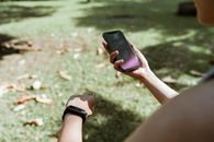 From above crop unrecognizable female wearing fitness tracker browsing modern mobile phone with blank screen while resting in green park