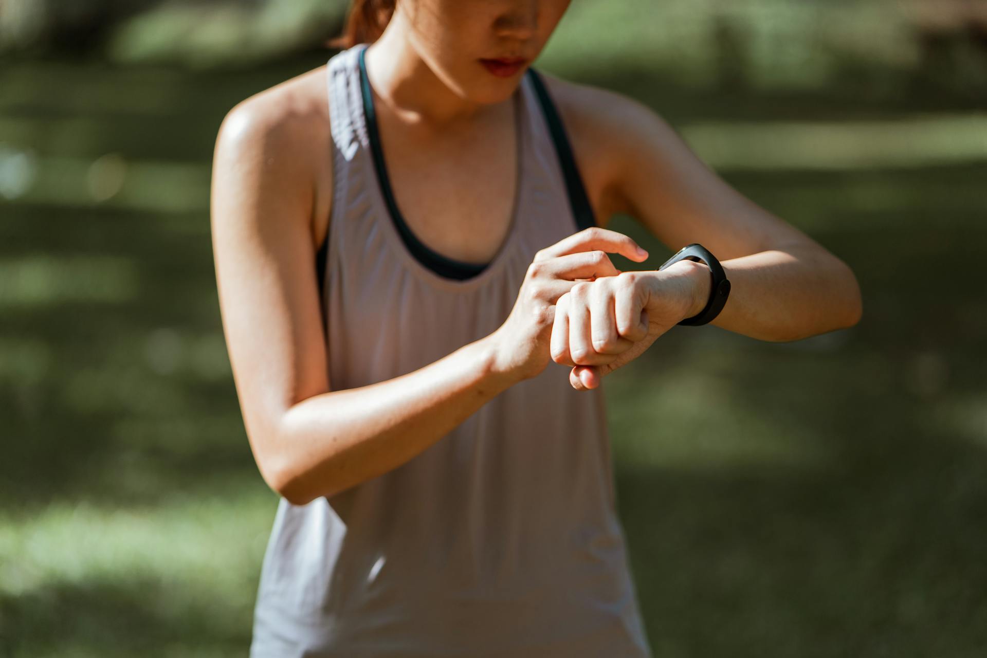 Crop fit sportswoman checking fitness tracker in nature