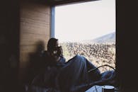 清晨，一位女士舒适地坐在大窗边，喝着咖啡，欣赏着窗外的自然景色